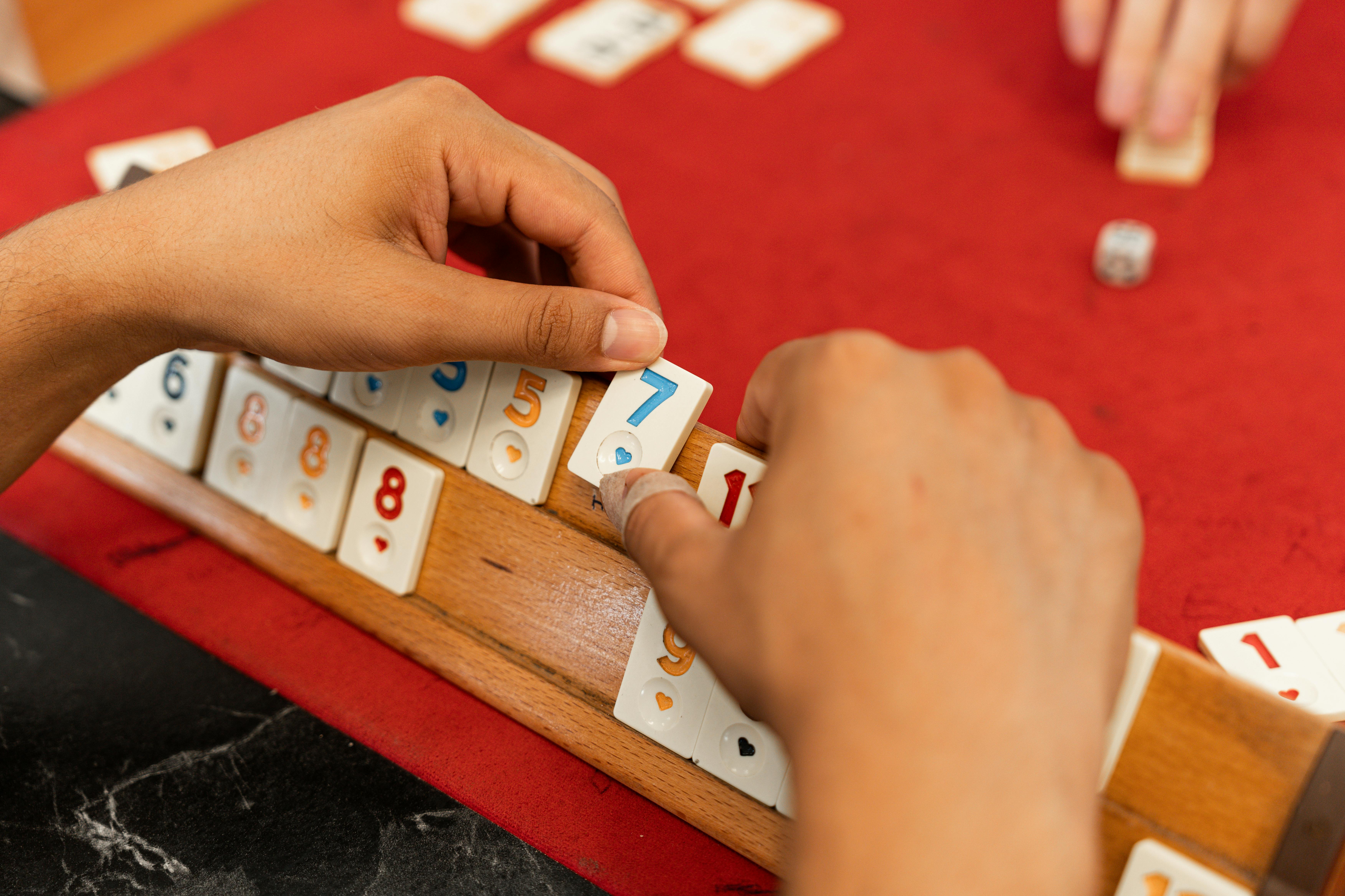 Hands arranging numbered tiles on a Rummikub board game set. Focus on strategy and gameplay.
